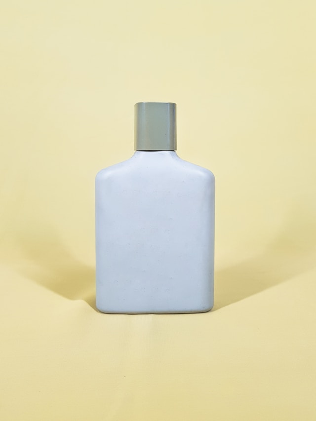 white perfume bottle with a grey cap in front of a light yellow background